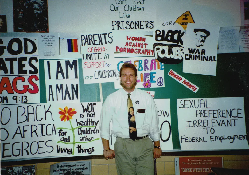 LGBT History Month founder Rodney Wilson standing near educational posters in his Missouri high school classroom, October 1994. Photo: [Msheble / Wikimedia Commons](https://commons.wikimedia.org/wiki/File:Rodney_Wilson_Standing_at_the_Poster_Project_(1994).jpg) (CC BY-SA 4.0)