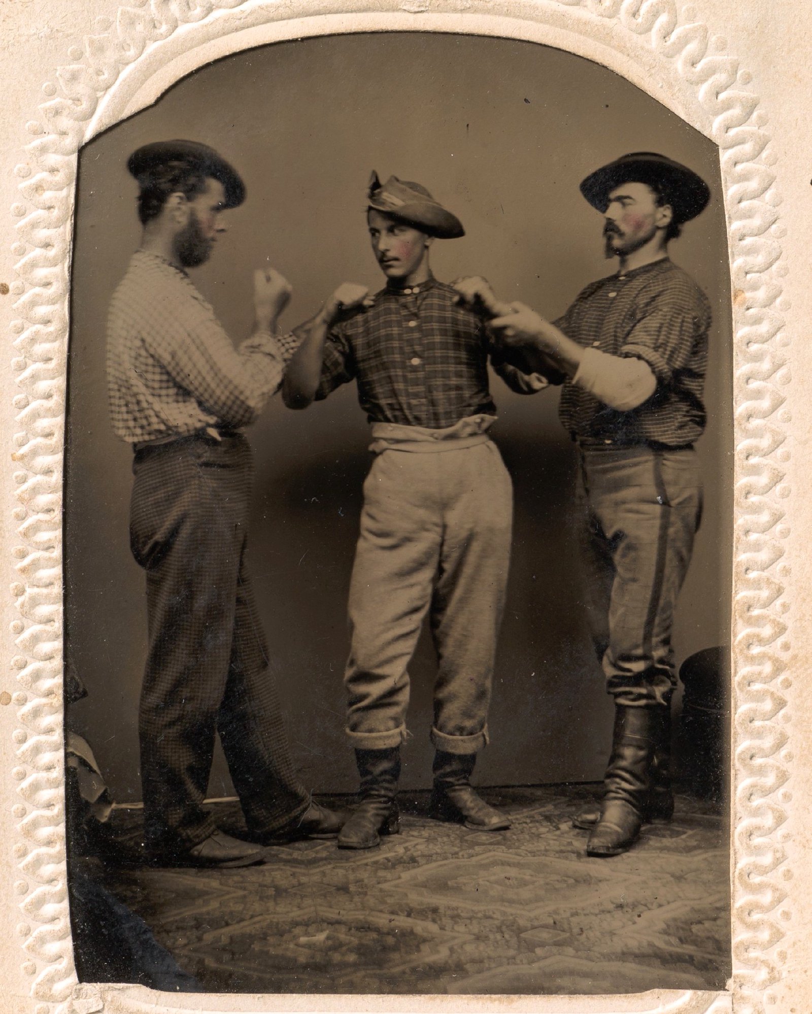 Dois homens em posição de boxe, um terceiro ajustando a postura de um deles; ferrotipia de J. C. Batchelder, décadas de 1860–1880