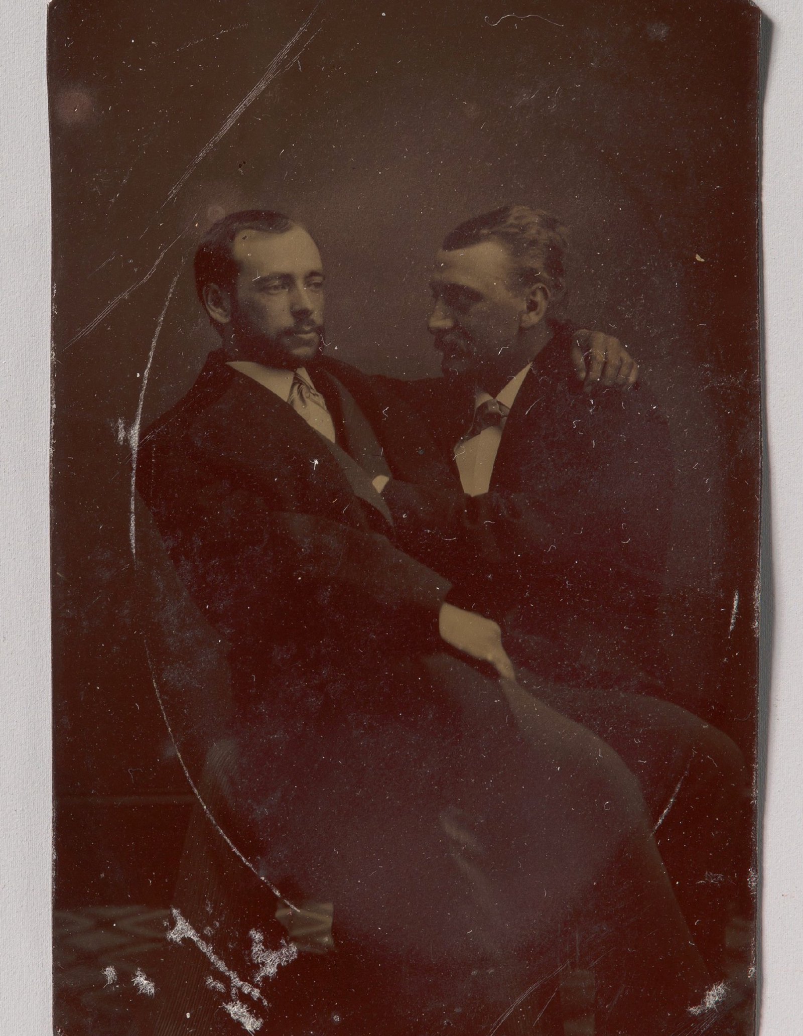 Dois homens sentados, um no colo do outro, com as mãos em posições sugestivas; ferrotipia de autor desconhecido, década de 1880