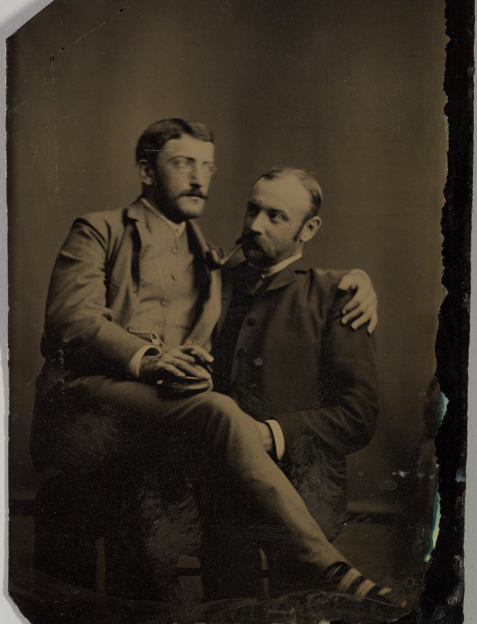 Dois homens a fumar, um sentado no colo do outro; ferrotipia de autor desconhecido, décadas de 1880–1890