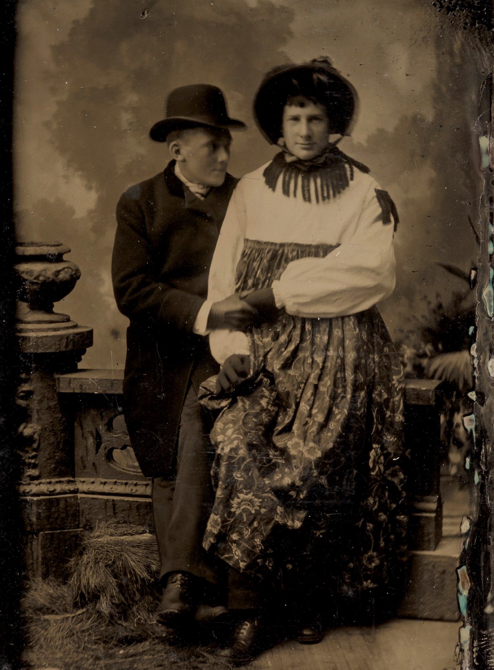 Dois homens, um deles vestido com roupa feminina, de mãos dadas; ferrotipia de autor desconhecido, décadas de 1870–1880